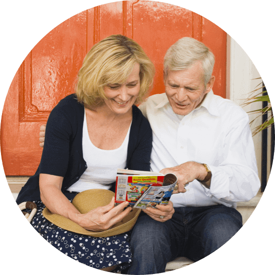 Symbolfoto: Eine Frau und ein Mann sitzen vor einer orange Tür und lesen eine Zeitschrift.