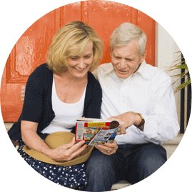 Symbolfoto: Eine Frau und ein Mann sitzen vor einer orange Tür und lesen eine Zeitschrift.